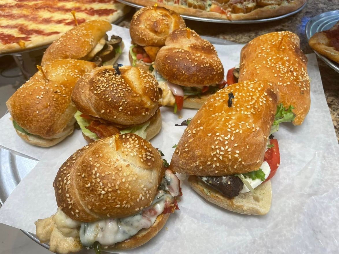 Tray of assorted sandwiches on glossy buns, topped with sesame seeds and filled with lettuce and meat.