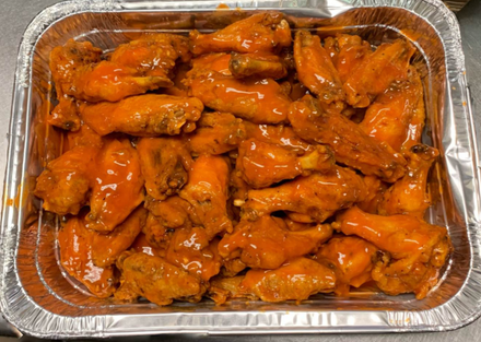 Tray of saucy buffalo chicken wings in a foil pan
