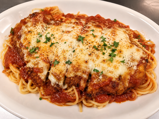 Spaghetti with meat sauce and melted cheese, garnished with parsley on a white plate