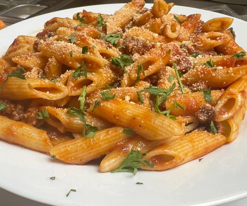 Plate of penne pasta in red sauce topped with herbs and grated cheese