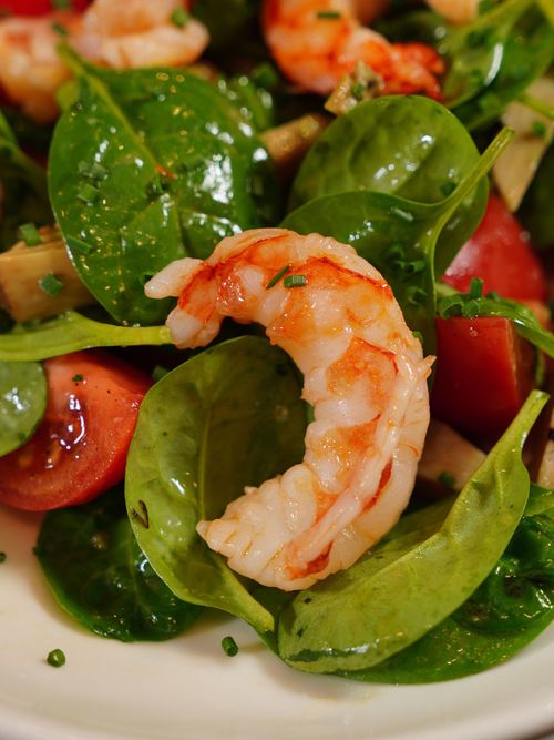 Shrimp salad with spinach, cherry tomatoes, and greens on a white plate