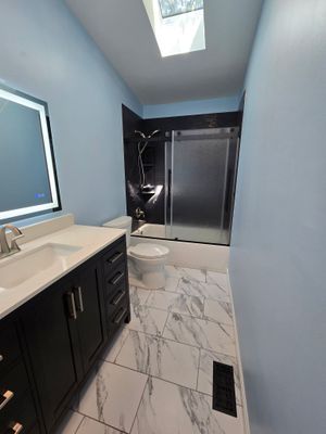 Empty beige living room with carpet, couch, wall photos, and a doorway to a lit hall