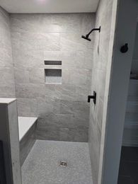 Tiled walk-in shower with two black shower fixtures and a built-in shelf niche