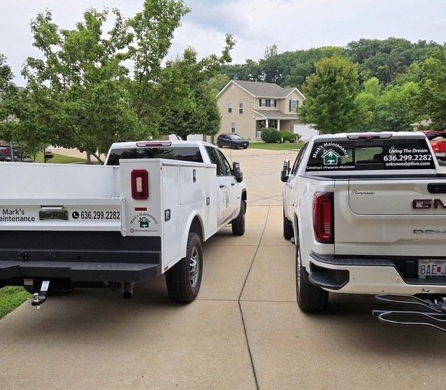 Two white pickup trucks parked in a driveway, with a house and trees in the background.