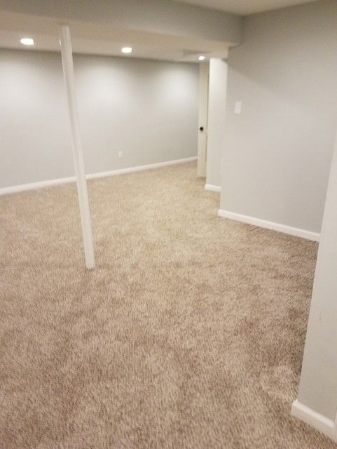 Empty carpeted room with light gray walls, white trim, and a support post in the foreground