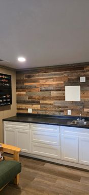 Modern kitchenette with white cabinets, black countertop, and wood-paneled backsplash in a cozy room