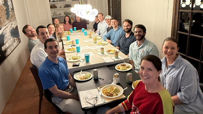 Group of young adults eating dinner sitting around a long table in a home
