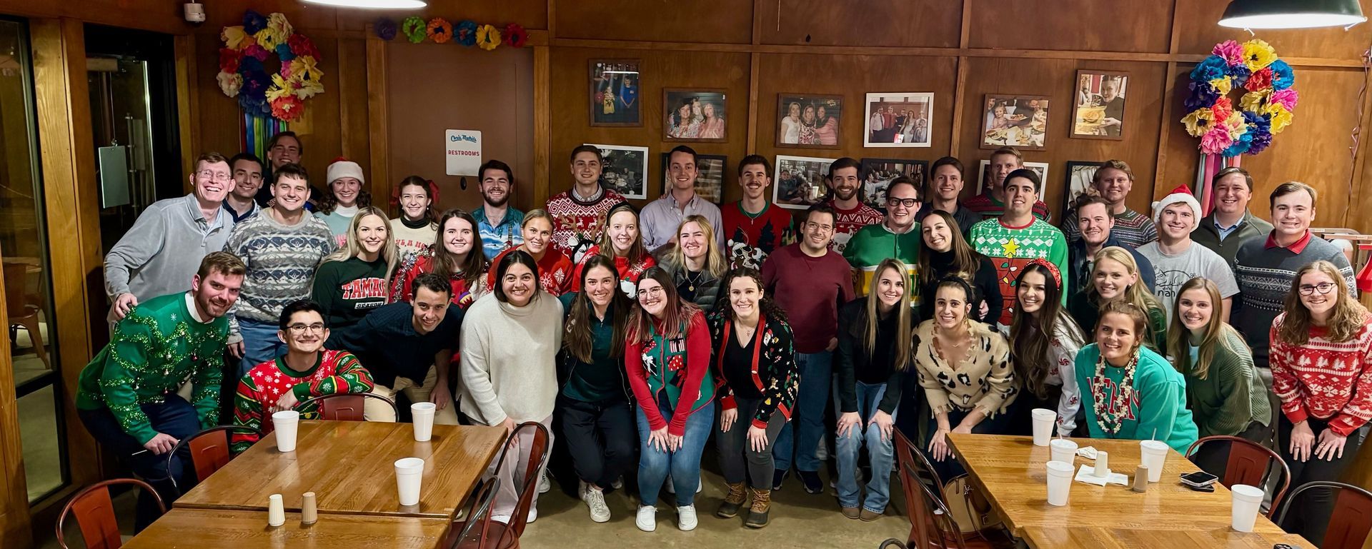 A large group of people posing for a photo at a festive indoor holiday party with decorations and wooden walls.