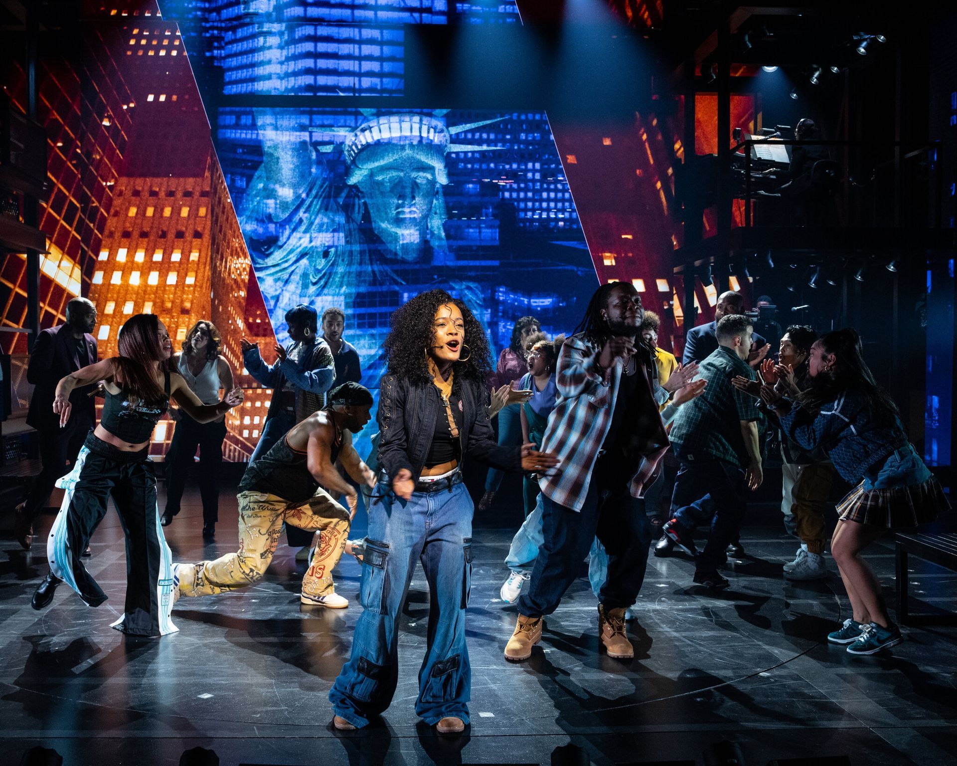A group of people are dancing on a stage in front of a statue of liberty.