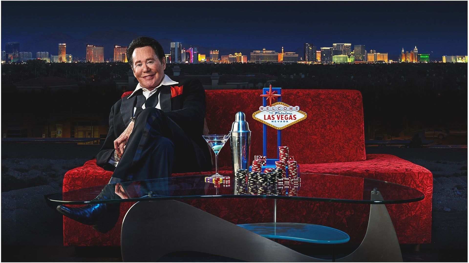 a man sits on a red couch in front of a las vegas sign