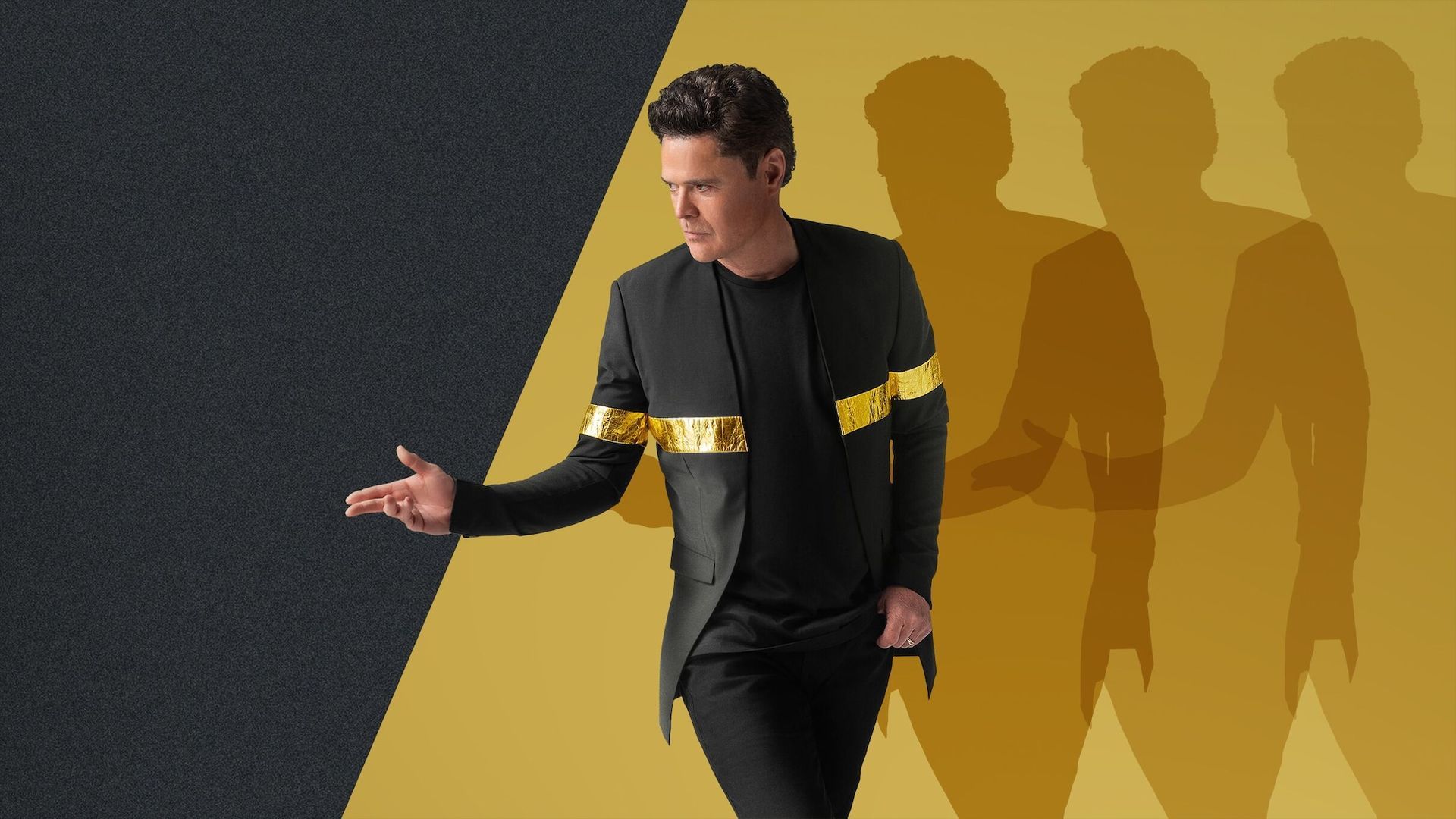 a man in a black suit is standing in front of a yellow wall .