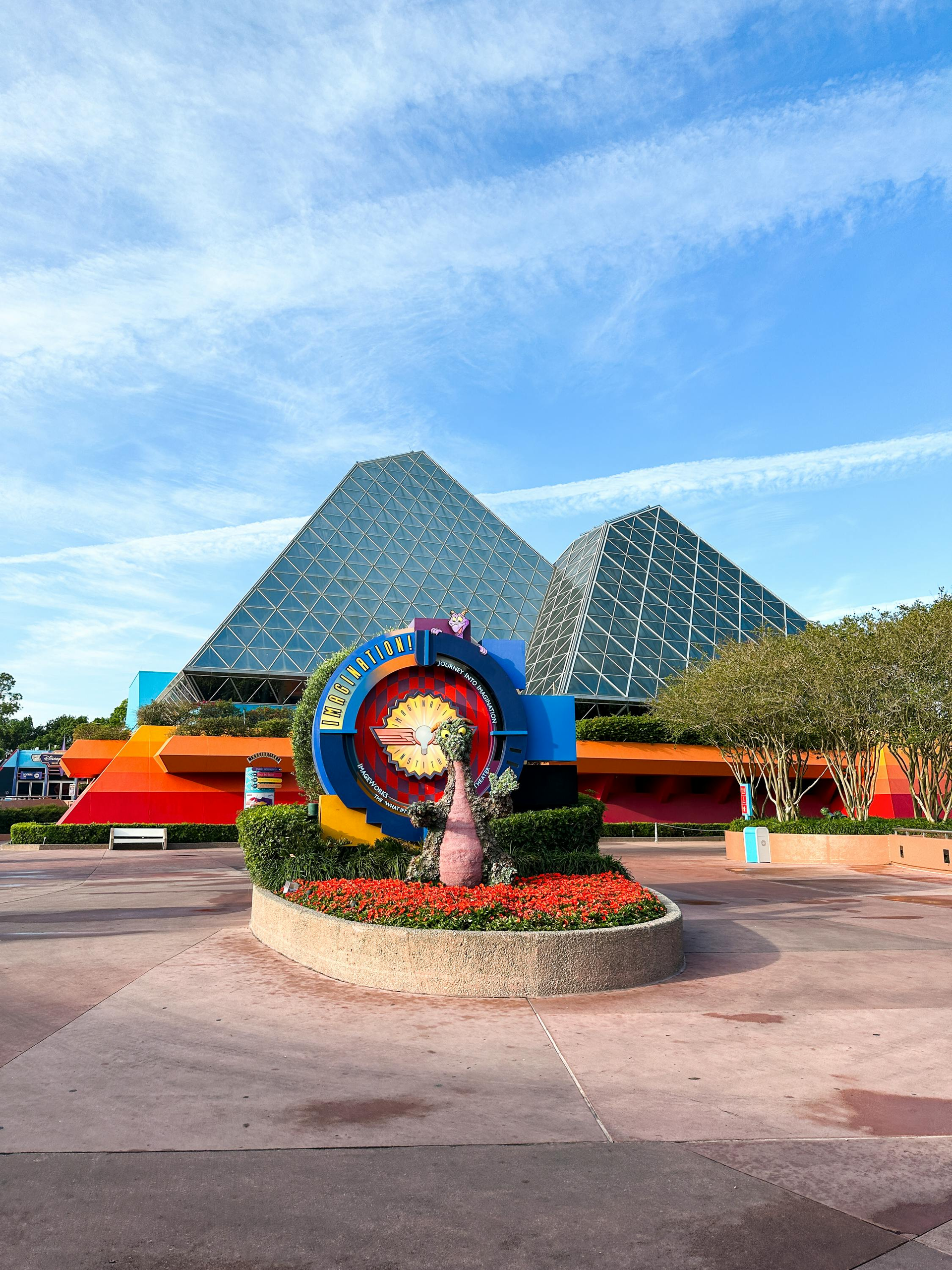 A colorful Disney character topiary sits in front of the uniquely geometric Journey into Imagination pavilion at Epcot.