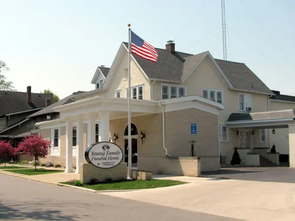 Funeral home with American flag flying, tan building with columns, sign in front.