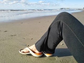 A person is sitting on the beach wearing flip flops