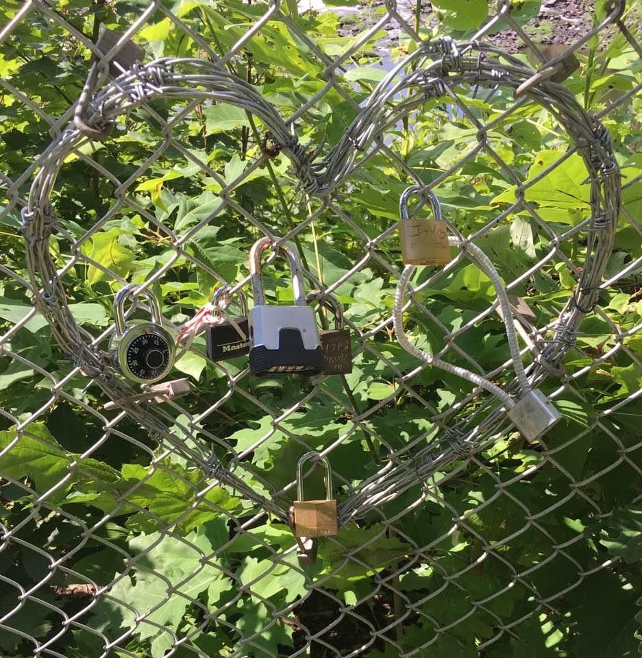 A chain link fence with locks in the shape of a heart.