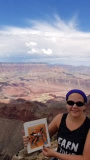 A woman is standing on top of a mountain holding a picture.