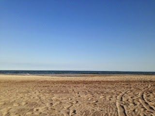 A sandy beach with a blue sky and the ocean in the background.