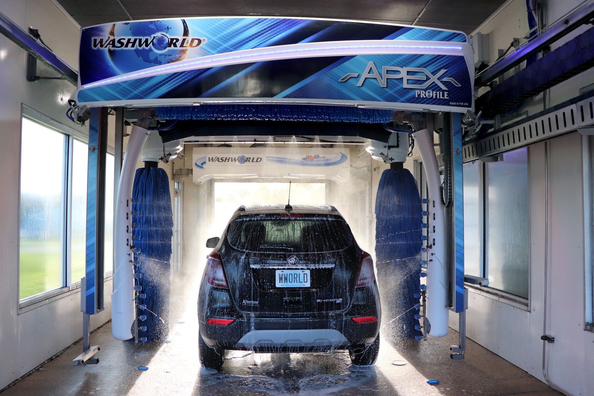 Black SUV inside an automatic car wash, being sprayed with water and soap.