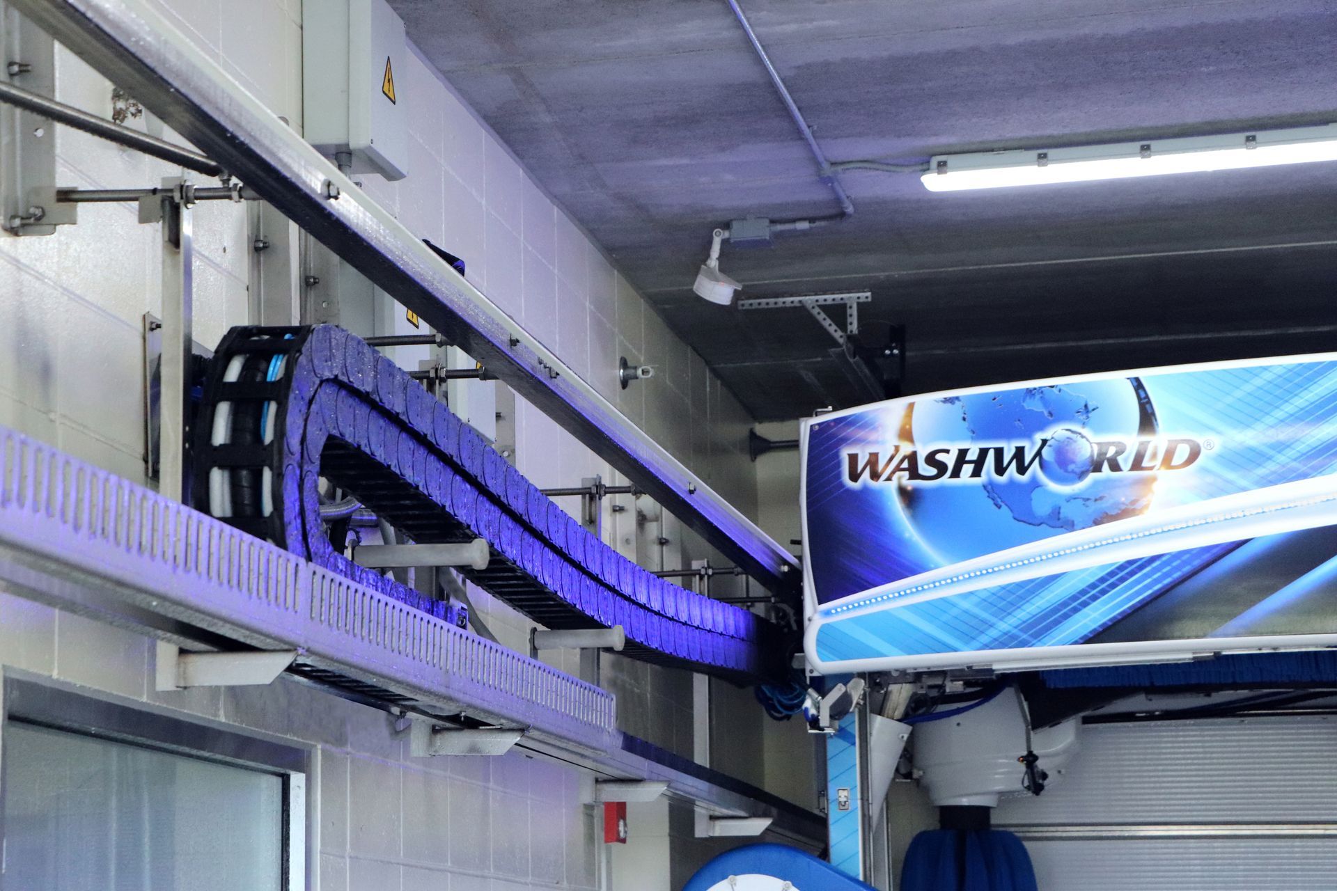 Car wash bay with blue brushes, "Washworld" sign, and overhead equipment.