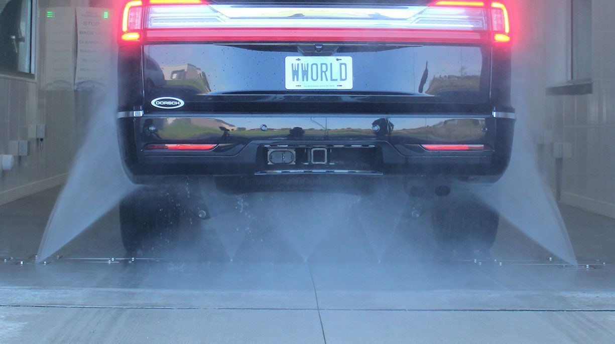 Black SUV in a car wash with water spraying the underbody of the vehicle.