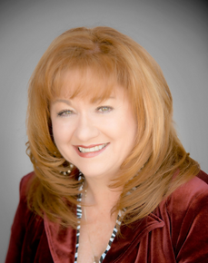 Portrait of a woman in a light blue button-up shirt, standing indoors with a neutral expression
