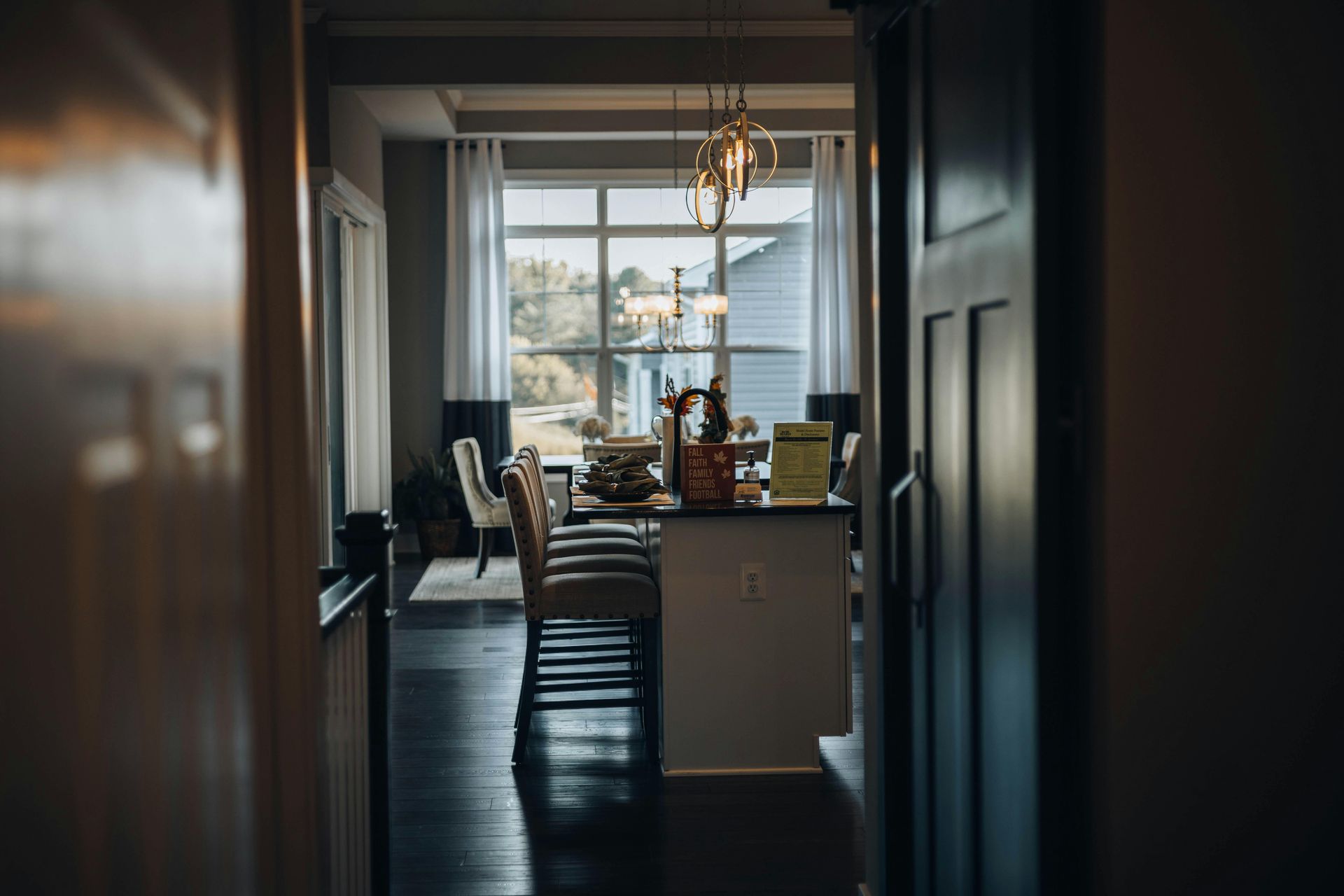 Dim kitchen hallway leading to a bright dining area with a table, chairs, and large window
