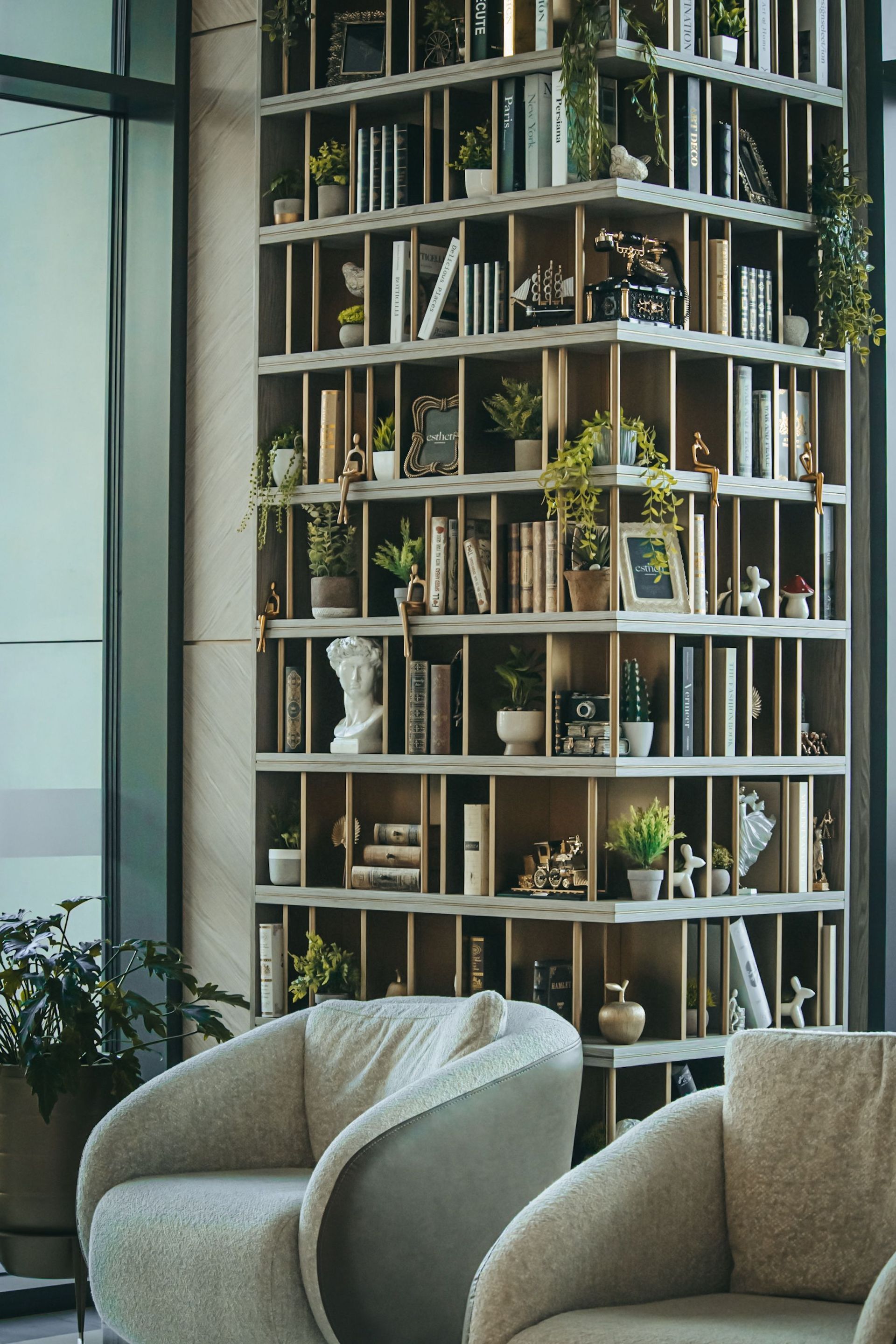 Modern lounge with gray chairs facing a tall bookshelf filled with books and plants