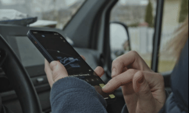 Person using a smartphone in a car, with the screen lit and a navigation map visible.