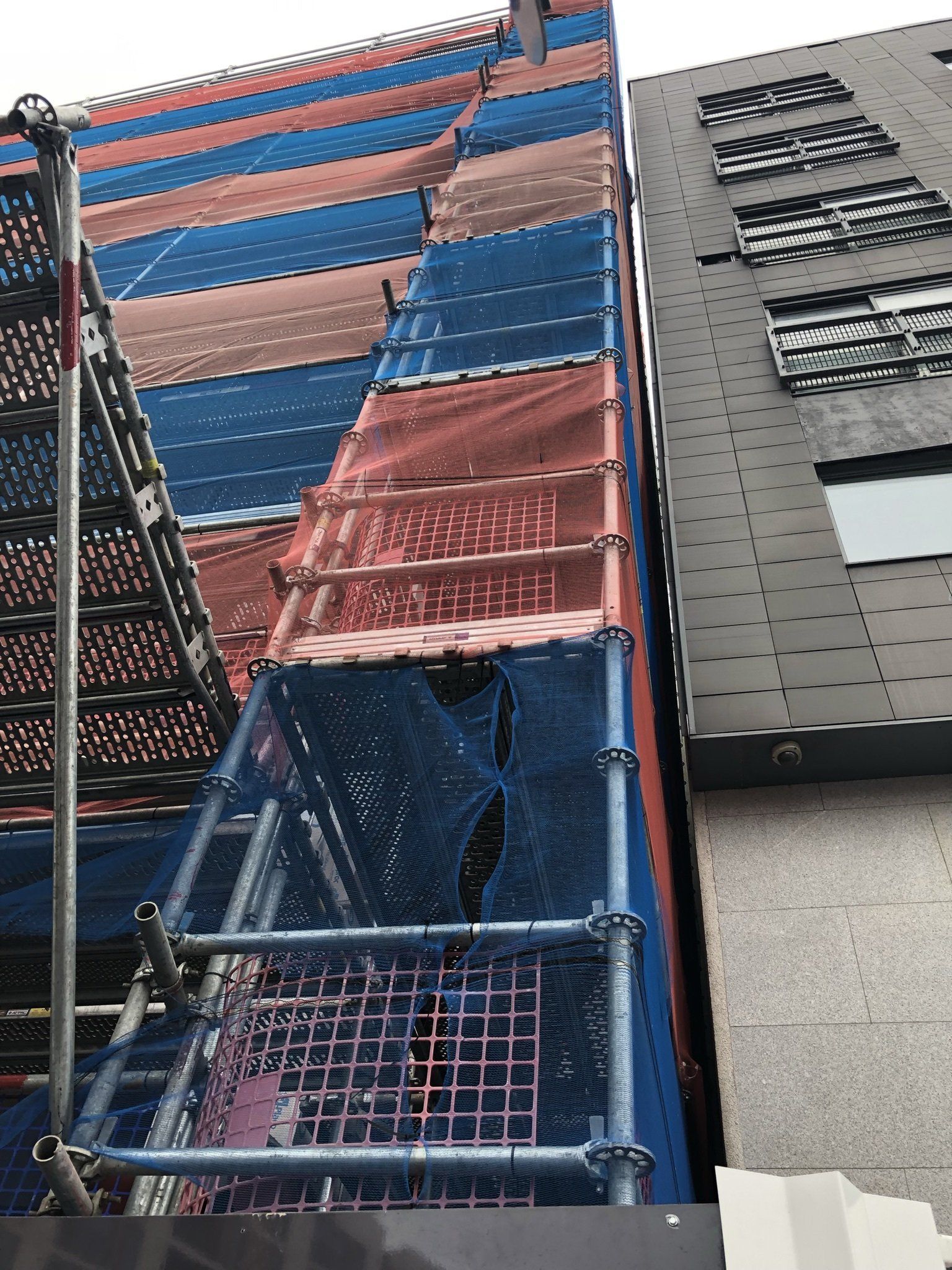 Tall colorful metal staircase beside a gray building facade