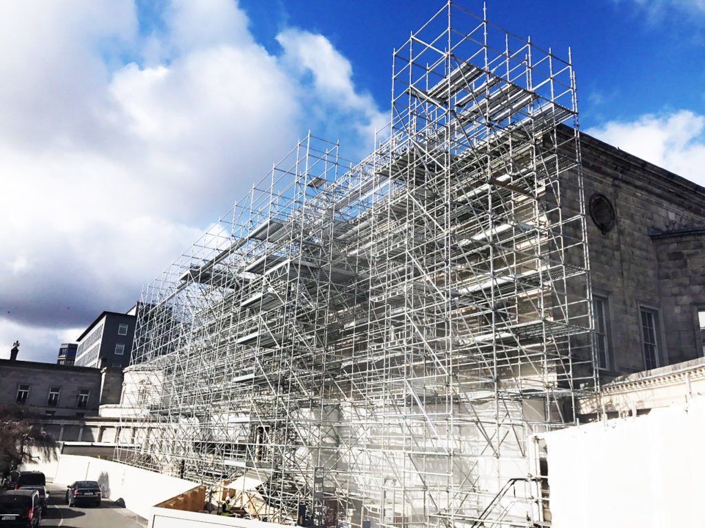 Large building covered in metal scaffolding under a partly cloudy sky