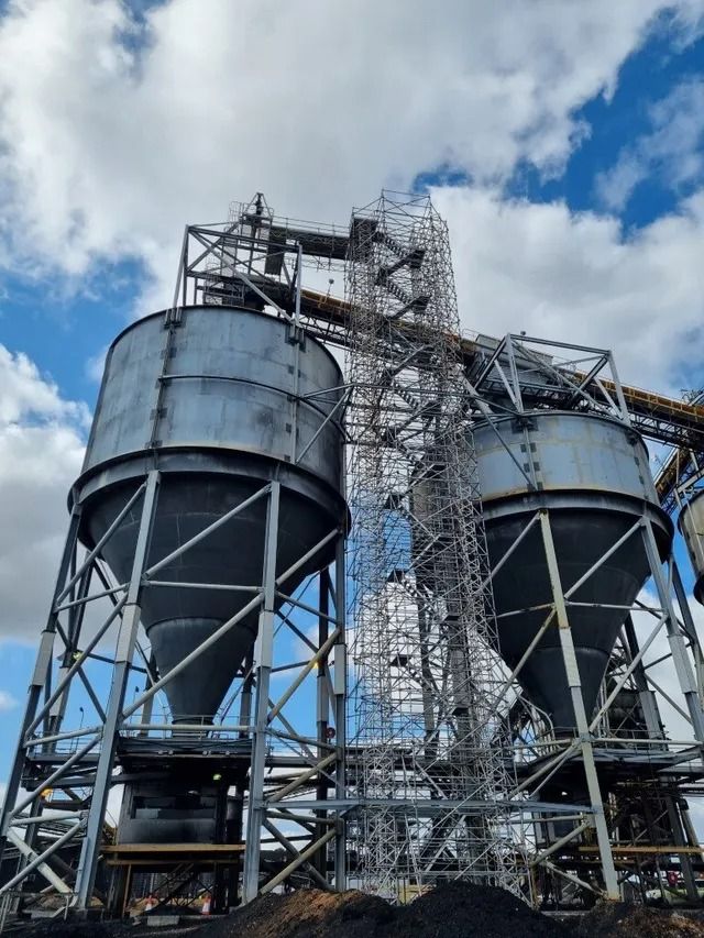 Industrial silos and steel conveyor tower under a cloudy blue sky