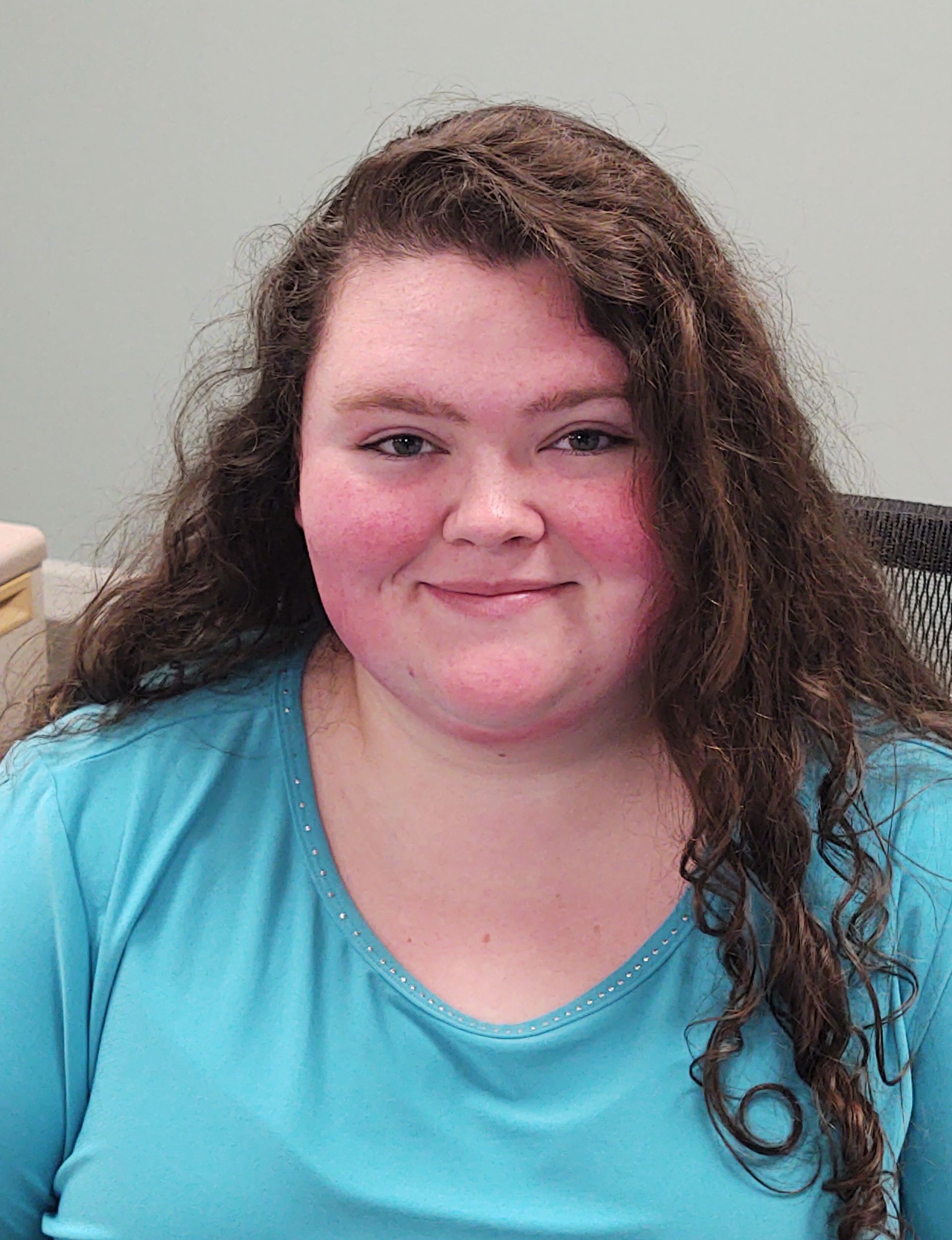 A woman with long curly hair is wearing a blue shirt and smiling for the camera.
