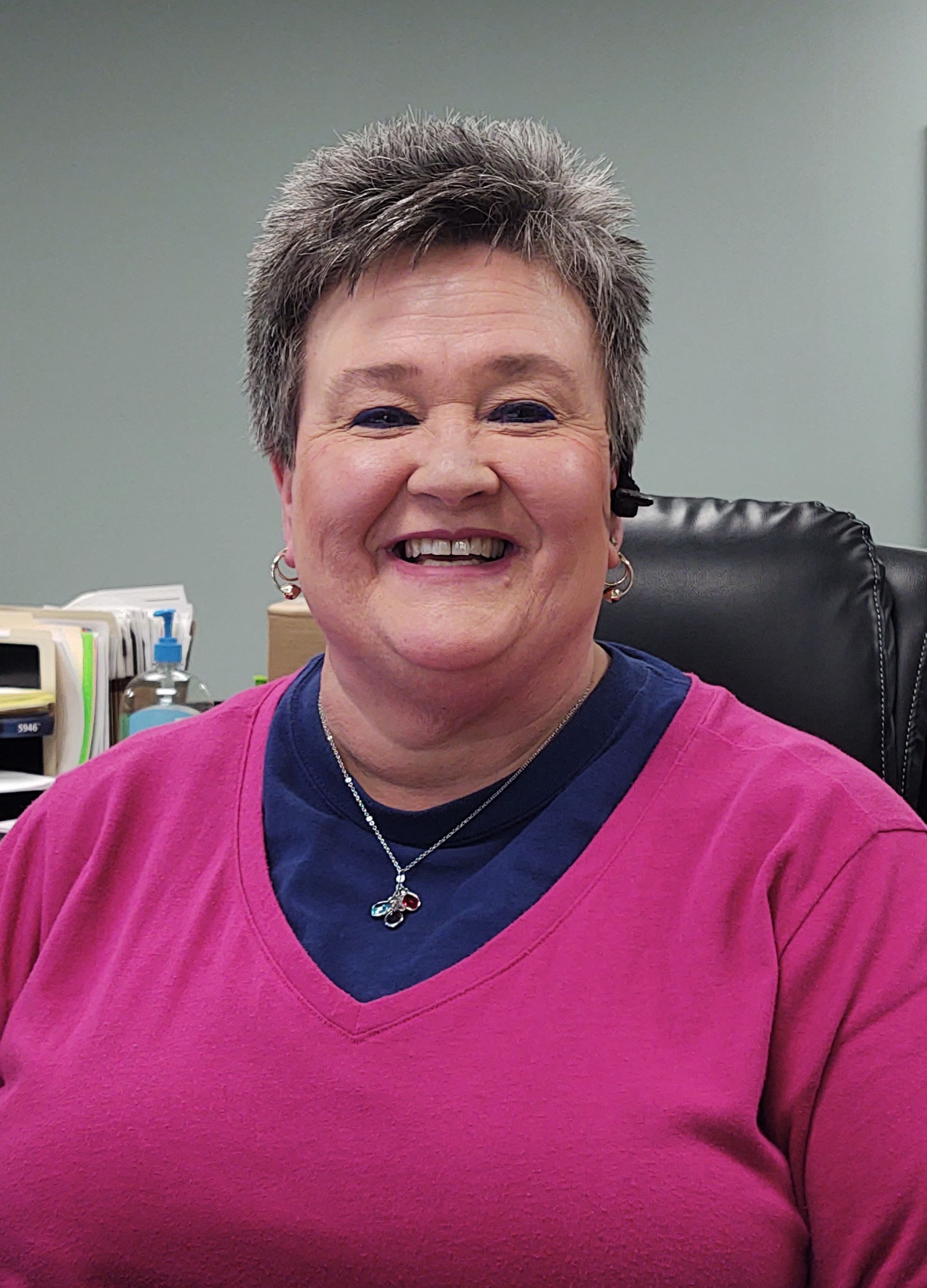A woman in a pink sweater is smiling while sitting in a chair.
