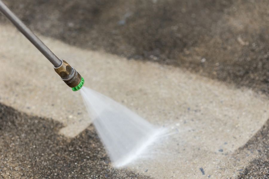 A hose spraying water onto a concrete surface, cleaning a wet patch on the ground.