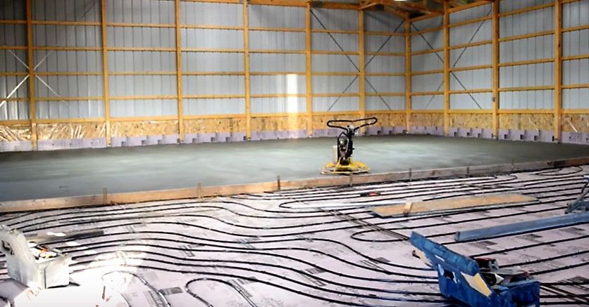 Large indoor industrial hall with a small machine smoothing a floor over marked insulation panels