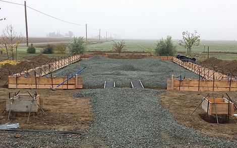 Gravel foundation with concrete footings and orange forms on a foggy rural construction site