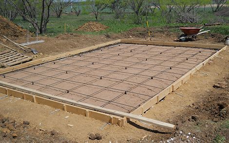 Concrete slab foundation under construction with rebar grid and wooden forms in a dirt lot