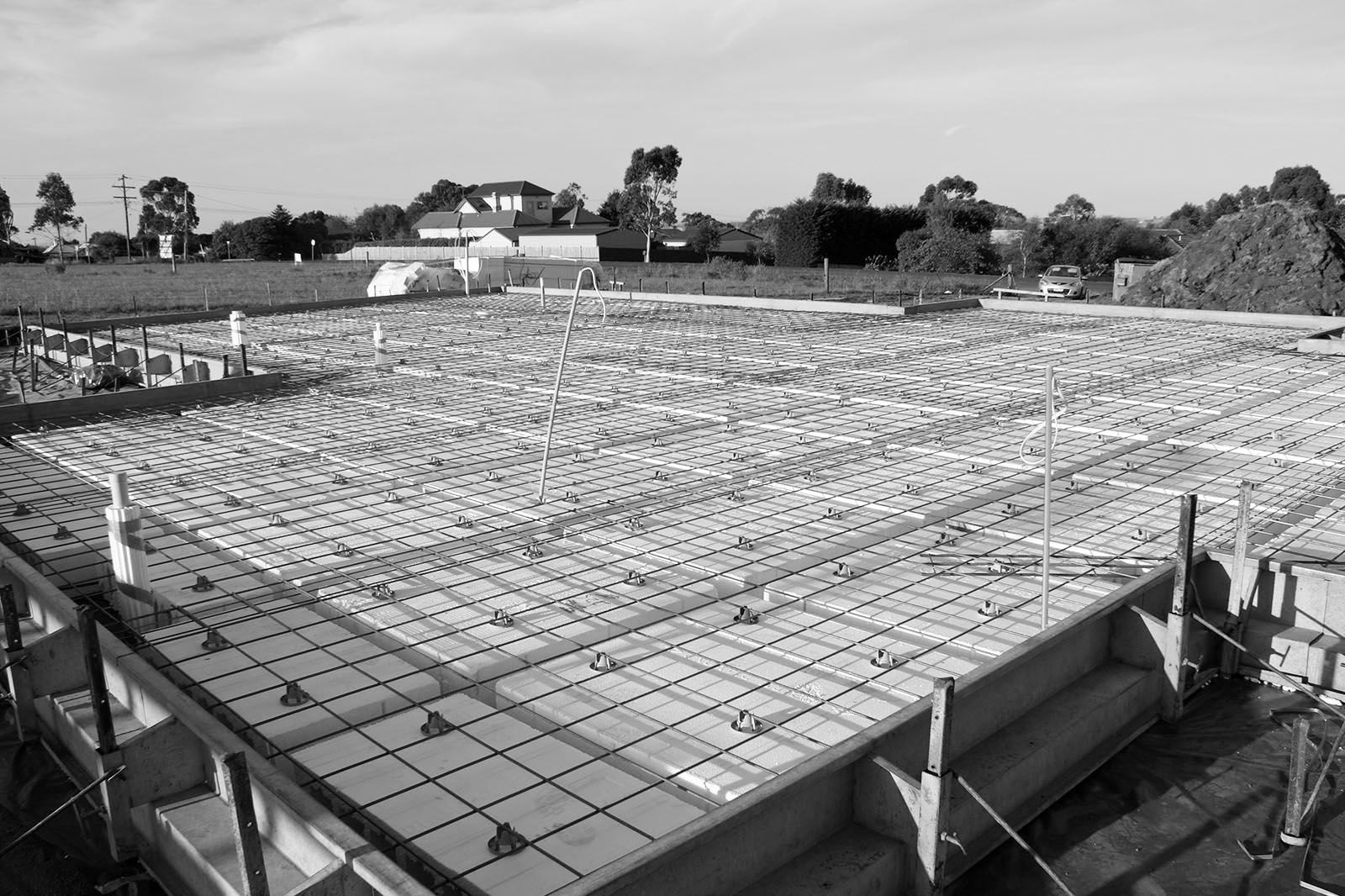 Concrete foundation slab under construction with rebar grid and formwork in an open field