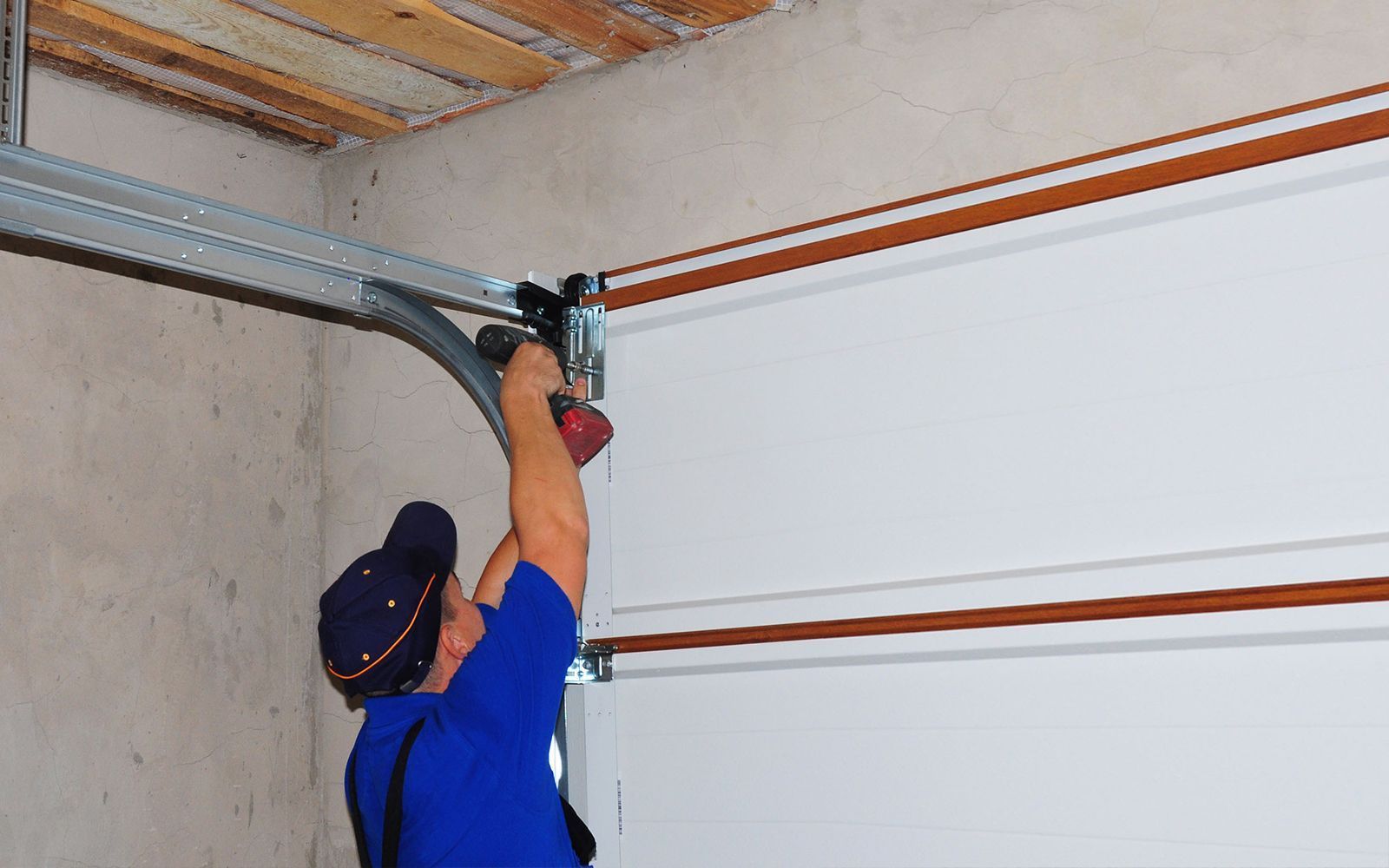 Worker in blue shirt installing a garage door opener on a white garage door ceiling