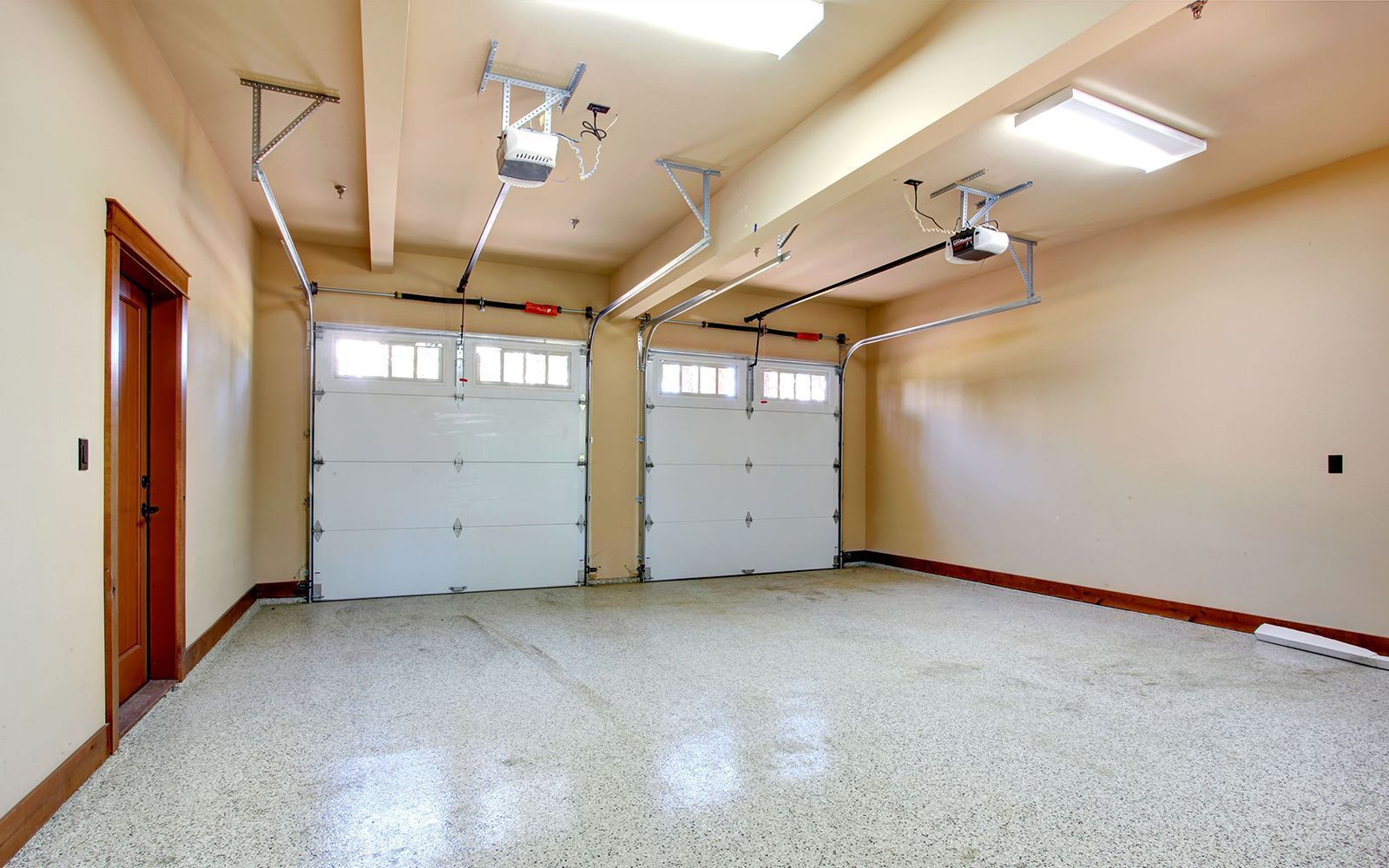 Empty garage with white speckled floor, beige walls, and two closed white garage doors.