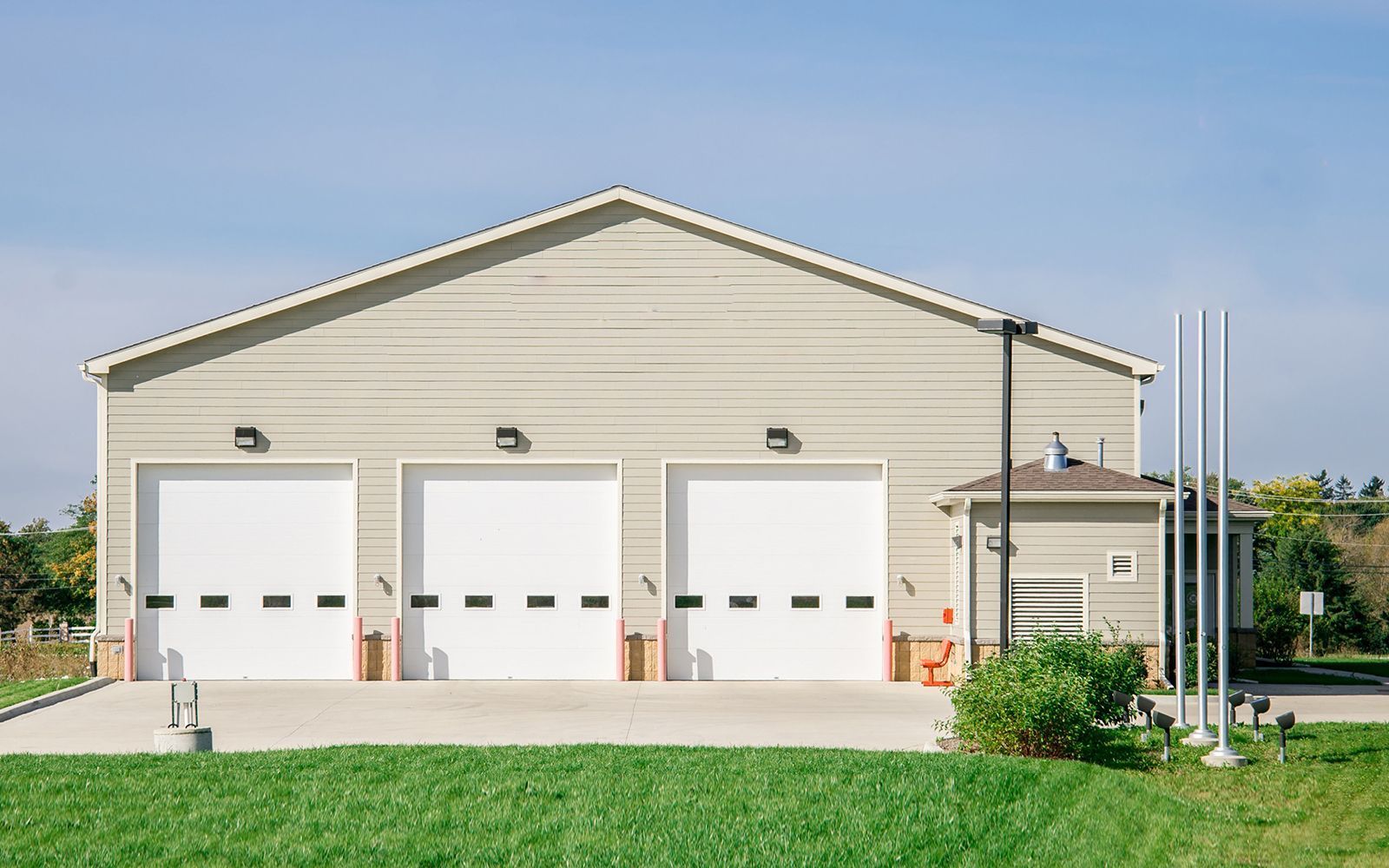 Three-bay beige garage with white doors and a small side shed on a sunny day