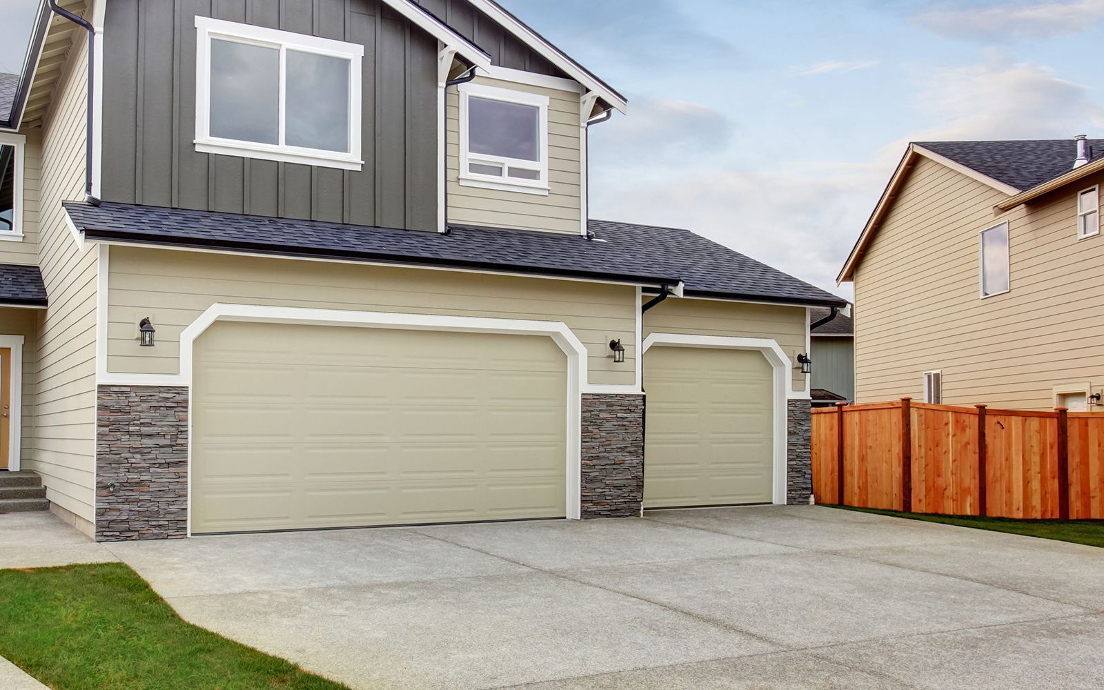 Suburban two-story house with beige siding, three garages, and a concrete driveway