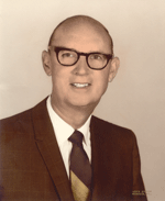 Bald man with glasses, smiling, wearing a suit and tie.