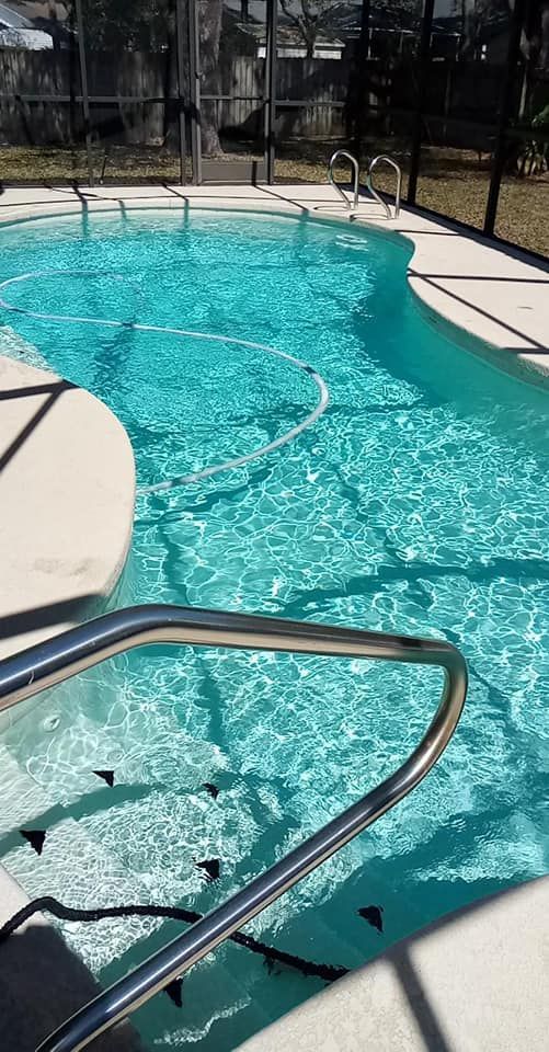 Pool with turquoise water, surrounded by light-colored concrete and a screened enclosure.
