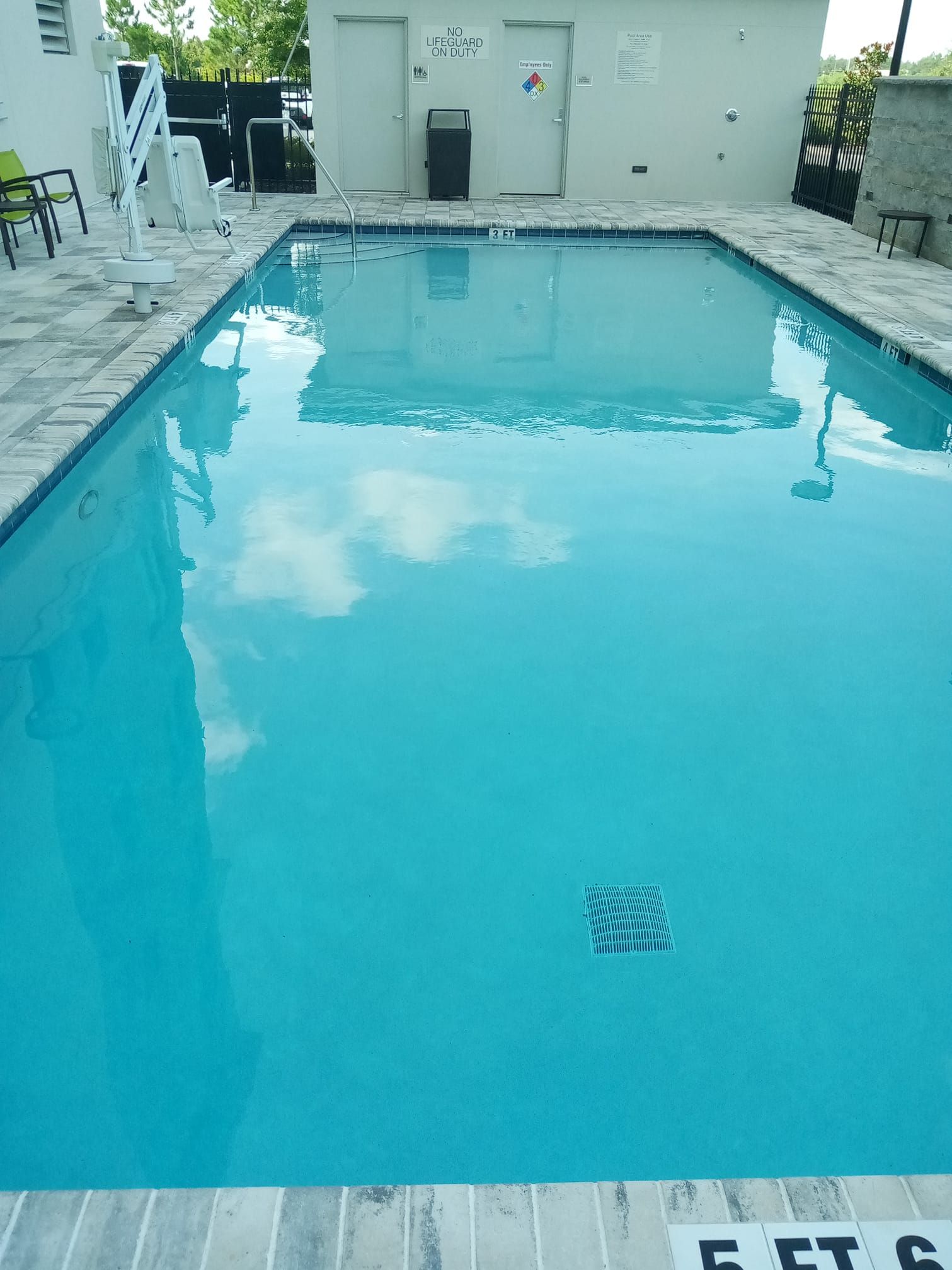 A rectangular, turquoise pool reflecting clouds. Light-colored tile surrounds the pool.