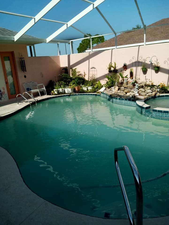 Swimming pool enclosed by a screen. Pink walls with plants and a small waterfall.
