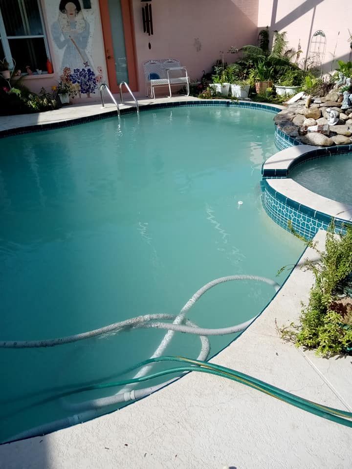 Pool with turquoise water, surrounded by concrete, plants, and a pink wall with a mural.