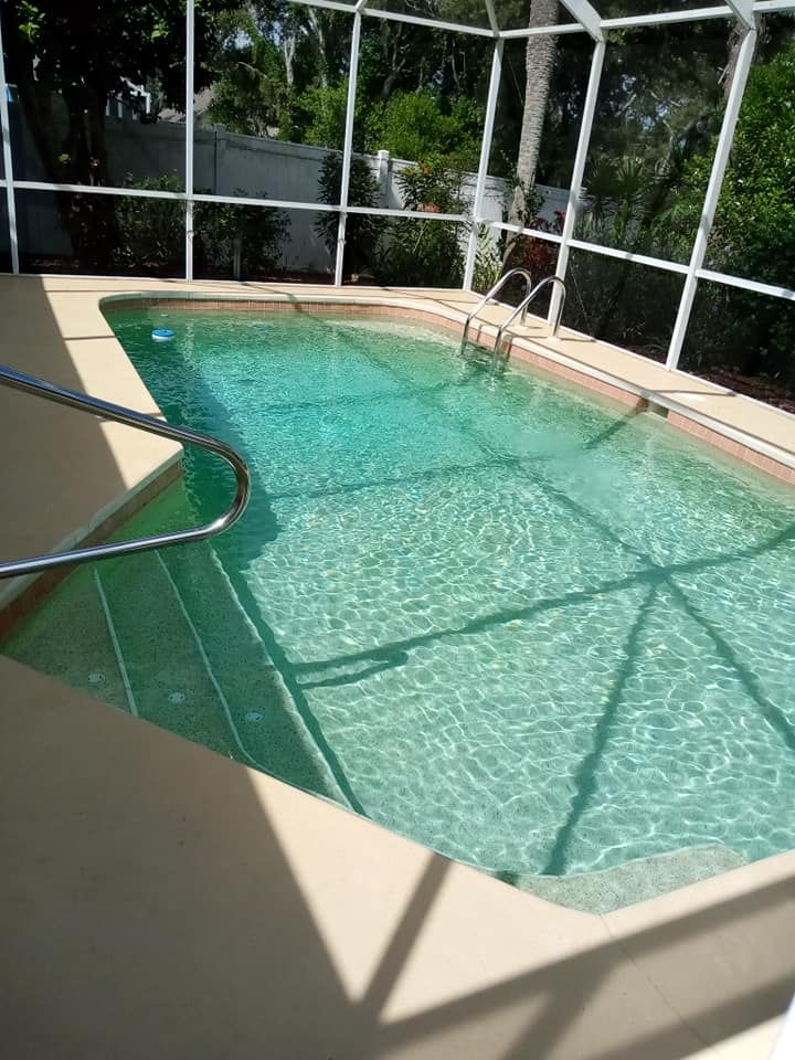 A rectangular pool with clear, turquoise water, enclosed by a screen. Concrete patio surrounds the pool.