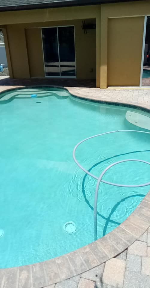 Swimming pool with turquoise water, a patio, and a building in the background.