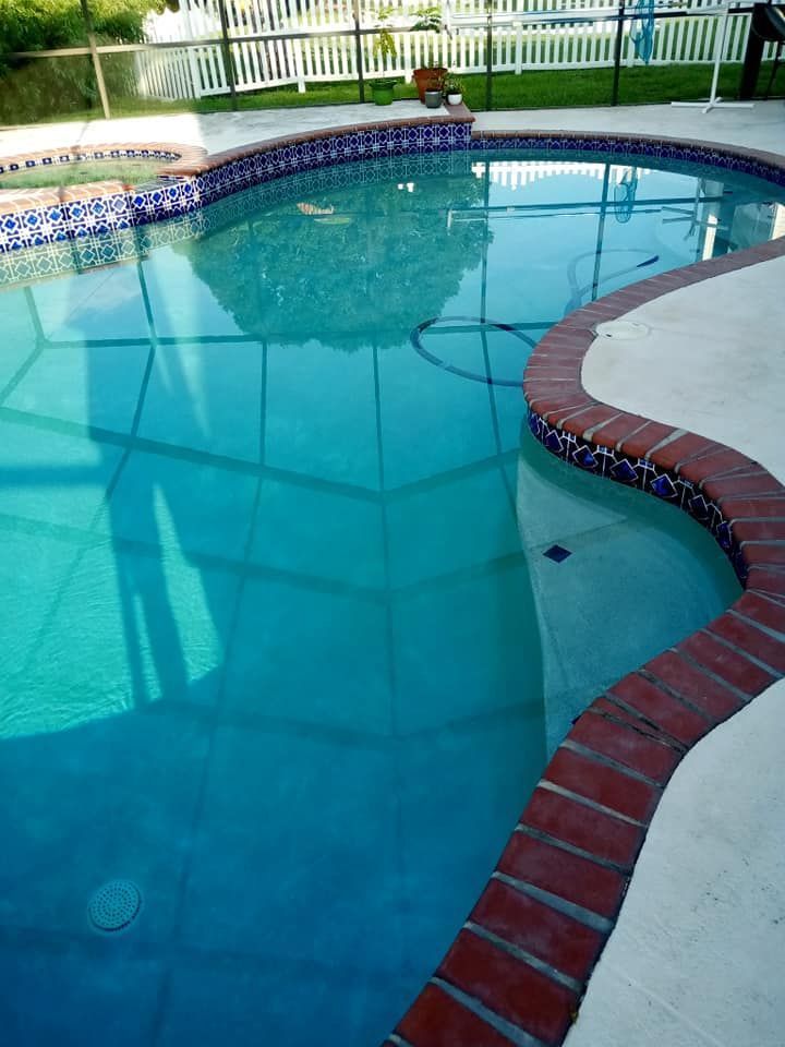 Pool with turquoise water, brick edging, and white fence in the background.